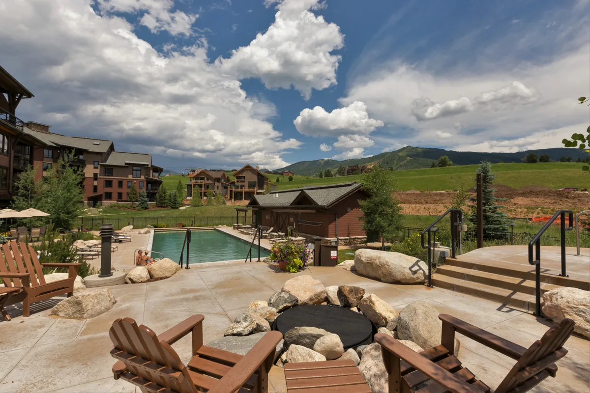 An expansive outdoor swimming pool surrounded by comfortable lounge chairs and a fire pit area, with a scenic mountain backdrop. The area is perfect for swimming, sunbathing, and social gatherings, offering a true resort ambiance.