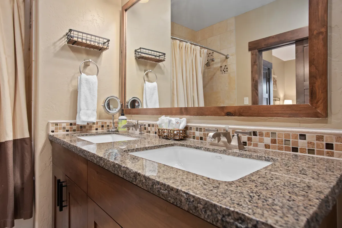 A spa-inspired bathroom with dual sinks set in a granite countertop, a framed mirror, and decorative tile backsplash. The organized and serene setting highlights premium materials and modern amenities.