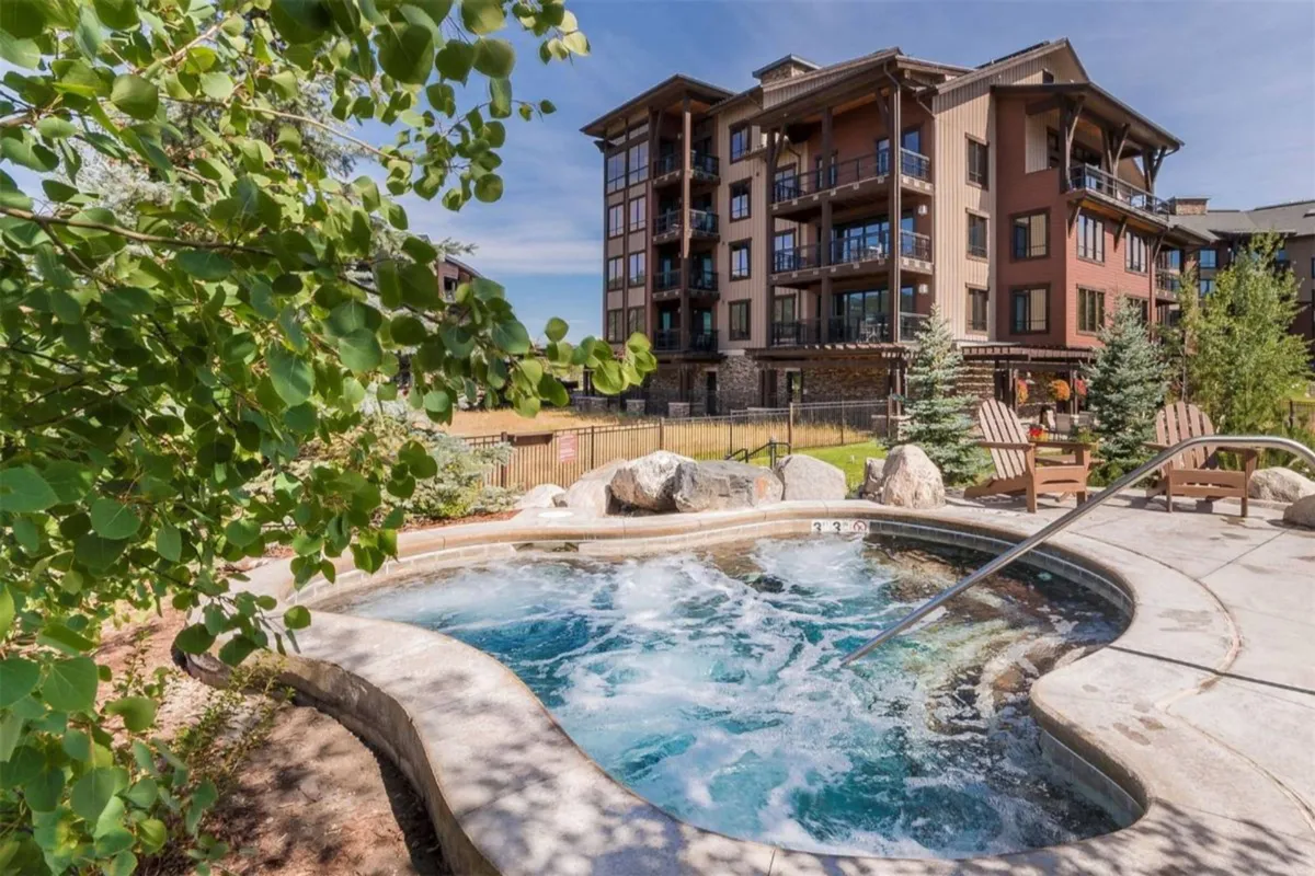 A tranquil outdoor hot tub nestled amidst greenery, with the building facade in the background. The area exudes a peaceful atmosphere, ideal for unwinding after a day of adventure, and suggests the soothing comfort of warm water and relaxation.