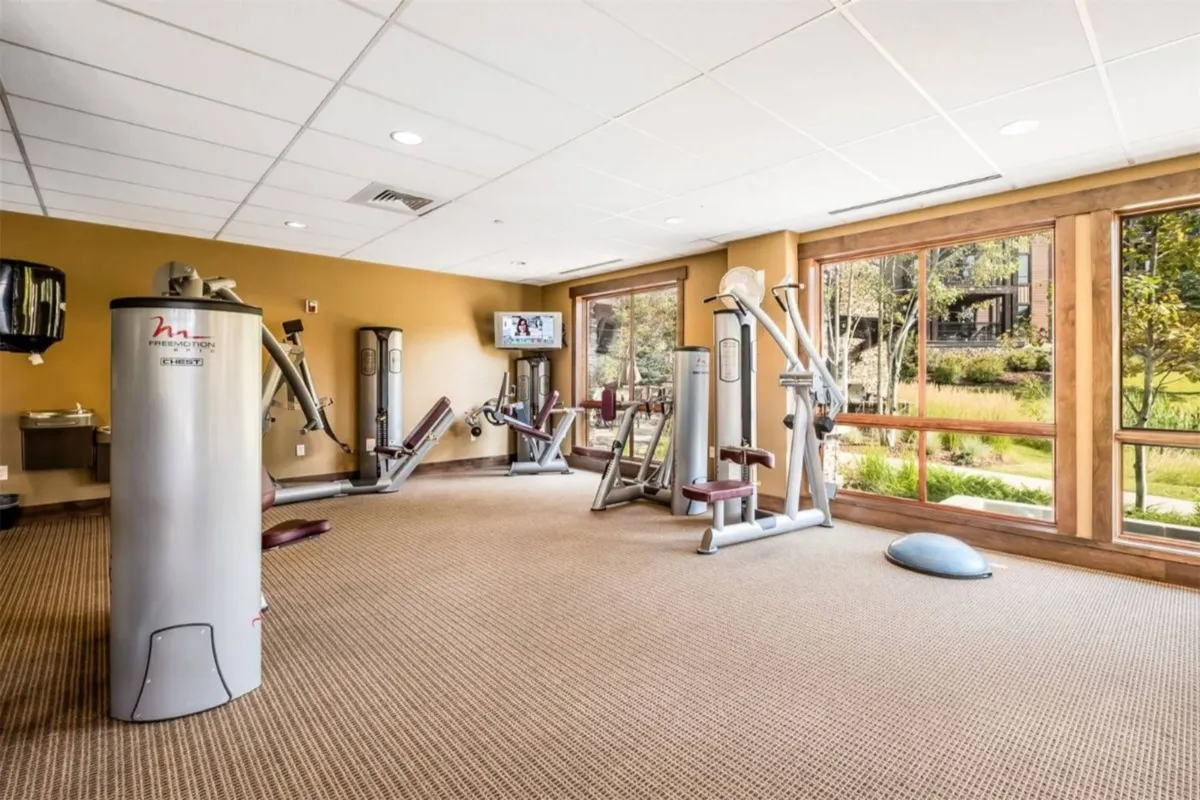 A modern fitness center filled with exercise machines, large windows bringing in natural light, and a mounted television screen. The atmosphere is bright and motivational, ideal for staying active during your stay.