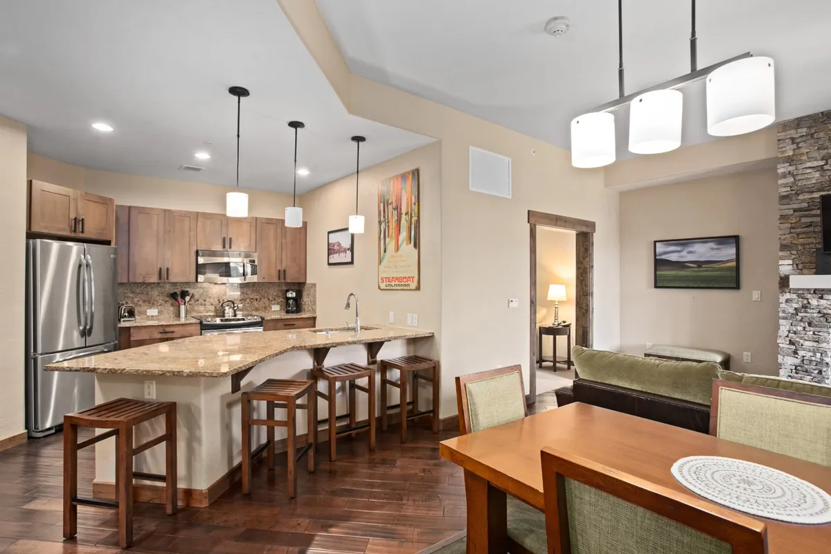 An open-concept space that seamlessly integrates a kitchen with a central island, a dining table set for meals, and a living area with comfortable seating and decorative artwork. The layout highlights ease of entertaining and daily living.