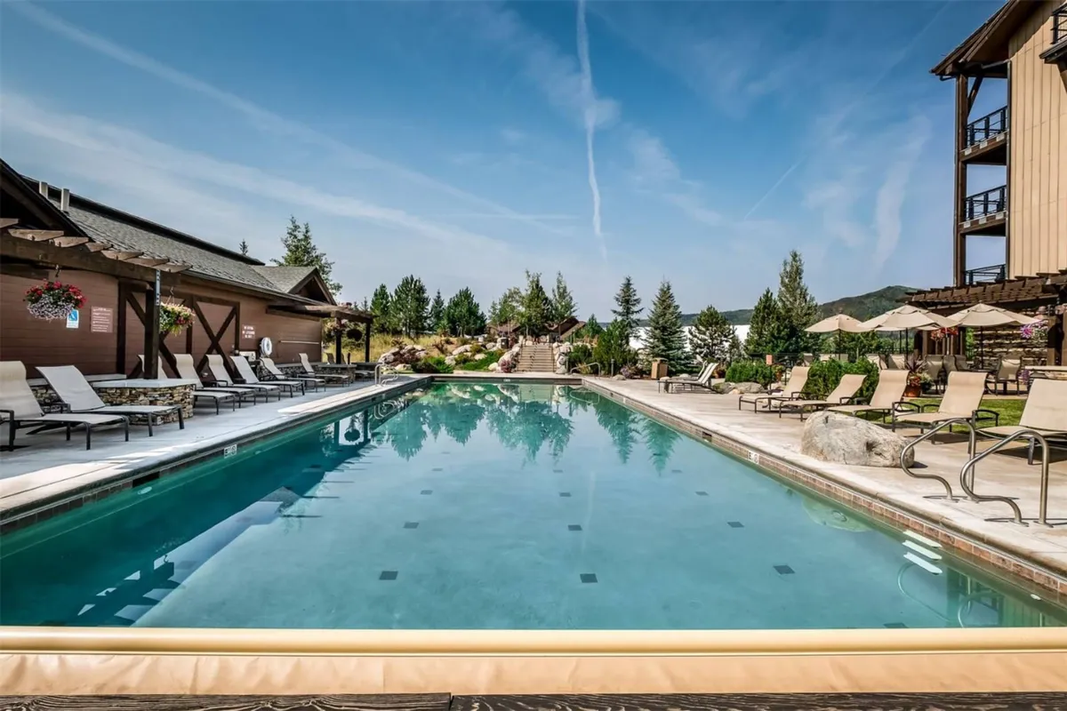 An inviting outdoor swimming pool surrounded by comfortable lounge chairs and lush landscaping, with the building structure visible in the background. The area is designed for both relaxation and recreation, ideal for sunbathing, swimming, and socializing in warmer months.
