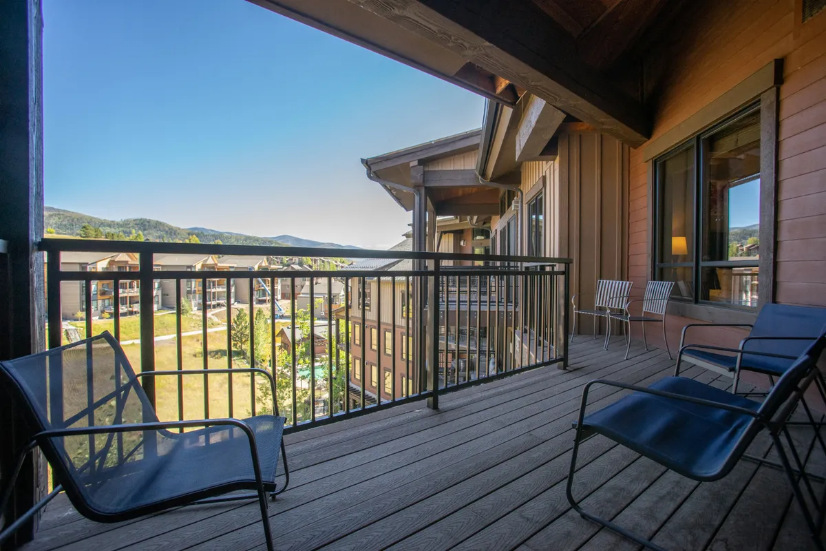 The image showcases the exterior of a penthouse condo in Steamboat Springs, Colorado, with a spacious balcony overlooking breathtaking mountain vistas. The balcony features comfortable seating, perfect for relaxing, enjoying sunrise coffee, or stargazing in the evening. The tranquil setting is ideal for socializing, taking in the natural beauty, or hosting family barbecues.